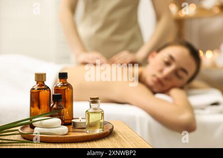 Aromaterapia. Donna che riceve un massaggio alla schiena nel salone spa, si concentra su bottiglie di oli essenziali, candele bruciate e pietre Foto Stock