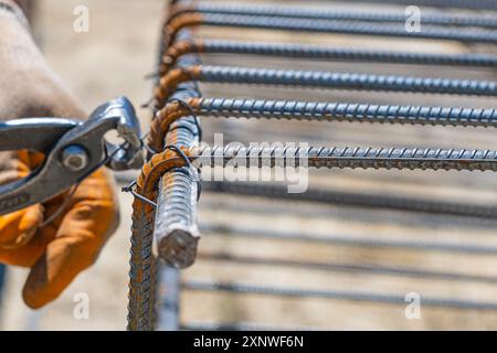 Un operatore utilizza un filo di legatura in acciaio per fissare le barre di acciaio alle barre di rinforzo. Primo piano. Strutture in cemento armato - lavorazione a maglia di un rinforzo in metallo Foto Stock