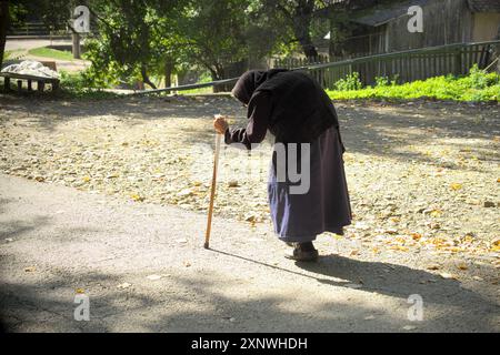 Una donna di cento anni cammina lentamente, piegata al bastone, il monastero di Vracevsnica, Gornji Milanovac, Serbia centrale (2) Foto Stock