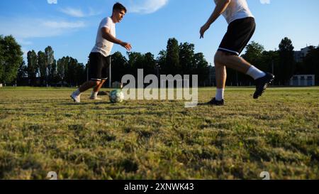 Due sportivi che giocano a calcio allo stadio al tramonto. Calciatori professionisti che eseguono trick con palla nel green Field. Giovani uomini che si allenano a. Foto Stock