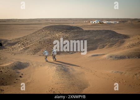 Due astronauti analogici partecipano ad una spedizione di simulazione su Marte nella regione del Dhofar, Oman. Questa immagine cattura l'esplorazione e l'arido paesaggio del deserto simile a Marte, rappresentando la curiosità umana e la ricerca della conoscenza. Foto Stock