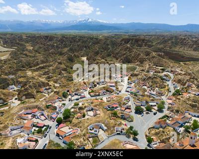 Vista panoramica di un villaggio incastonato in un paesaggio roccioso e collinare con montagne sullo sfondo, vista aerea, abitazioni nelle grotte, quartiere delle grotte Foto Stock