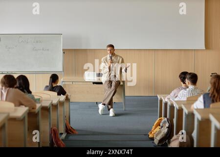 Riprese grandangolari di insegnanti maschi adulti che insegnano agli studenti di diritto civile parlando con microfono portatile in classe universitaria con lavagna bianca e spazio di copia Foto Stock