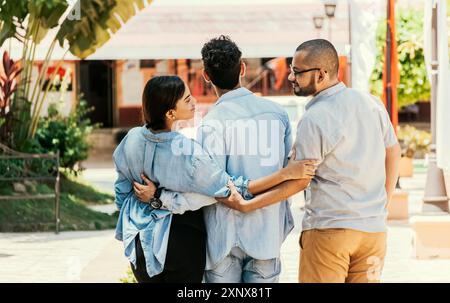 Ragazza infedele che cammina nel parco con il suo ragazzo mentre tiene un altro uomo per mano. Donna che si tiene per mano con un altro uomo mentre cammina con lei Foto Stock