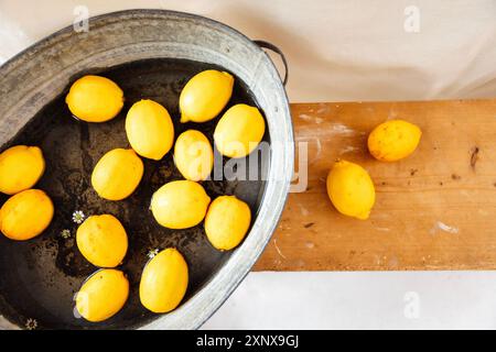 Succosi limoni freschi e margherite in acqua in una vasca in metallo vintage. Vista dall'alto. Panca retrò in legno con agrumi gialli. Tessuto bianco nel backgrou Foto Stock