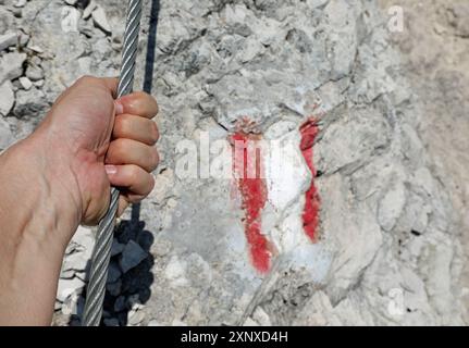 mano dell'arrampicatore che afferrano saldamente il cavo d'acciaio di una ferrata in alta montagna in estate Foto Stock