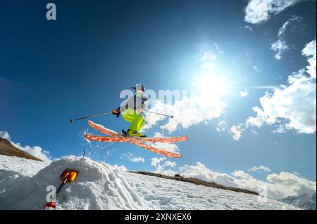 Ragazza sciatrice in volo dopo essere saltata da un kicker in primavera sullo sfondo di montagne e cielo blu. Primo piano con grandangolo. Il concetto di Foto Stock