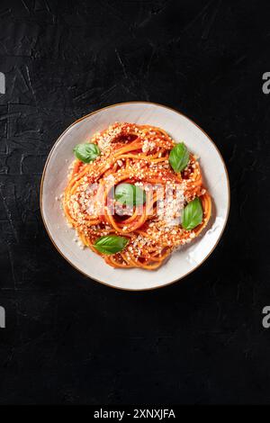 Spaghetti con salsa di pomodoro, parmigiano e foglie di basilico fresco, sparati dall'alto su sfondo scuro con un posto per il testo Foto Stock