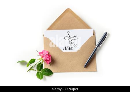 Salva l'indicazione della data su un invito in una busta marrone kraft, girato dall'alto su uno sfondo bianco con una rosa Foto Stock