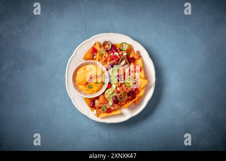 Nachos messicani con peperoncino con carne, guacamole e salsa al formaggio, top shot su sfondo blu Foto Stock