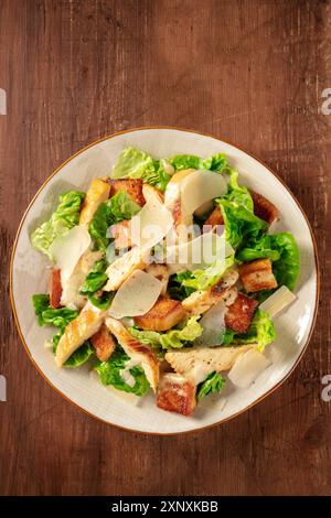 Caesar Salad con pollo alla griglia, foglie di insalata verde e parmigiano, sparata dall'alto su uno sfondo rustico scuro in legno Foto Stock