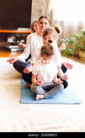 Donne adulte e bambine che si siedono in fila sul pavimento e si stendono le braccia mentre si fa yoga a casa insieme Foto Stock