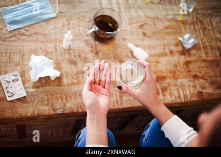 Angolo alto di donna anonima con pillole e tazza d'acqua che strega a tavola con tè e mela durante la malattia Foto Stock