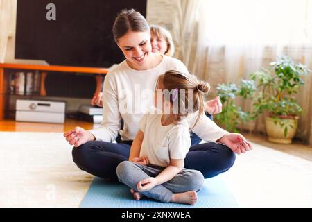 Donne adulte e bambina che si siedono in fila sul pavimento mentre fanno yoga a casa insieme Foto Stock