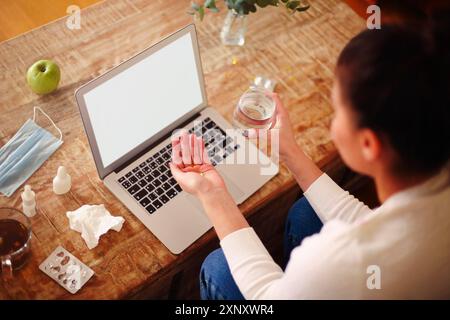 Angolo alto di femmina con pillole e tazza d'acqua che strega a tavola con tè e mela durante la malattia Foto Stock