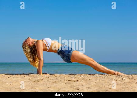 Giovane caucasica che pianse indietro sulla spiaggia per l'esercizio di yoga Foto Stock