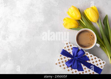 Scatola regalo per tulipani gialli con nastro blu e una tazza di caffè sul tavolo in pietra grigia, vista dall'alto, spazio per la copia a disposizione piatta Foto Stock