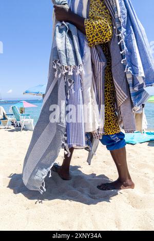 Spiaggia venditrice drappeggiata in asciugamani colorati sulla spiaggia di Sandy Foto Stock