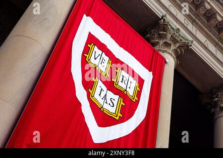 Cambridge, Massachusetts, USA - 24 giugno 2022: Primo piano del logo dell'Università di Harvard su uno striscione rosso appeso a un edificio. Il logo è uno scudo W. Foto Stock