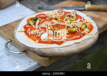 Pizza fresca integrale con salsa di pomodoro, broccoli, cipolle e formaggio, preparata per la cottura su un tavolo da cucina in legno, cibo vegetariano sano Foto Stock