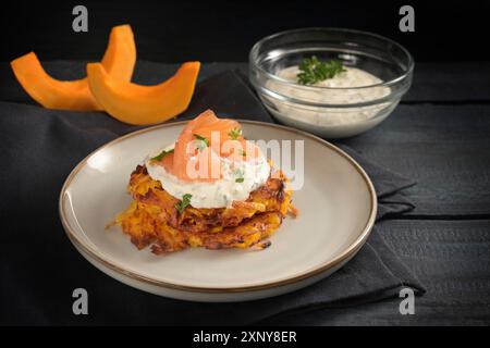 Frittelle di zucca rossa kuri con formaggio spalmabile alle erbe e salmone affumicato, spuntino autunnale vegetale per il Ringraziamento e Halloween su un piatto grigio e un Foto Stock