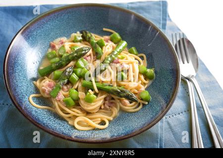 Spaghetti carbonara con asparagi verdi su un piatto blu con tovagliolo e posate, fuoco selezionato, stretta profondità di campo Foto Stock