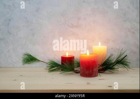 Tre candele accese per il terzo Avvento, ramo di pino come una decorazione semplice e minima su un asse di legno chiaro contro una parete rustica in gesso, grande copia Foto Stock