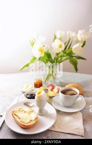 Tavolo per la colazione con fiori, panini, uova cucinate, caffè e molto altro, servito con amore la domenica, il compleanno, la festa della mamma, sullo sfondo chiaro Foto Stock