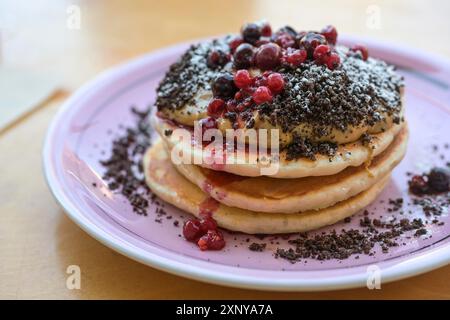 Pancake impilati con crema al burro di arachidi, frutti di bosco, crumble e zucchero a velo su un piatto, colazione dolce, brunch o piatto da dessert, concentrazione selezionata Foto Stock