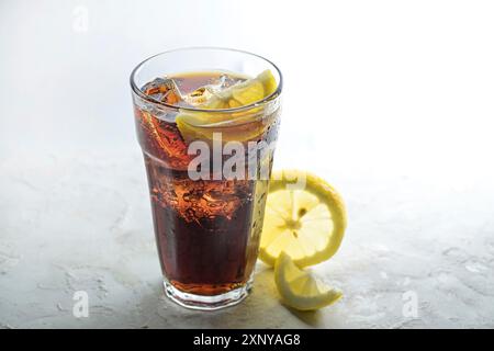 cola fresca con cubetti di ghiaccio e fette di limone in un bicchiere da bere, bevanda dolce a base di caffeina su sfondo grigio chiaro, copia spazio, messa a fuoco selezionata Foto Stock