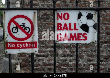 Due cartelli di divieto su una recinzione metallica, uno contro il ciclismo e l'altro contro le partite a palla Foto Stock