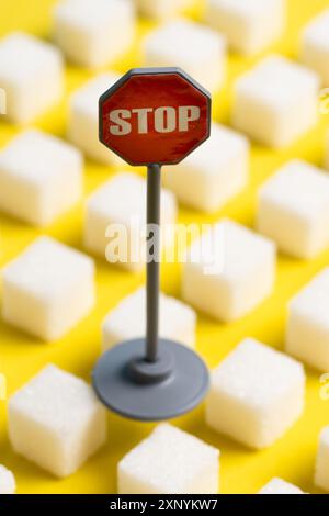 Segnale di stop e cubetti di zucchero su sfondo giallo, immagine concettuale Foto Stock