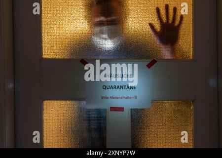 Immagine simbolica quarantena domestica, l'uomo è in isolamento a casa a causa di una sospetta infezione corona, segnale di avvertimento per i visitatori sulla porta d'ingresso Foto Stock