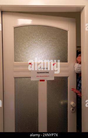 Immagine simbolica quarantena domestica, l'uomo è in isolamento a casa a causa di una sospetta infezione corona, segnale di avvertimento per i visitatori sulla porta d'ingresso Foto Stock