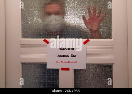 Immagine simbolica quarantena domestica, l'uomo è in isolamento a casa a causa di una sospetta infezione corona, segnale di avvertimento per i visitatori sulla porta d'ingresso Foto Stock