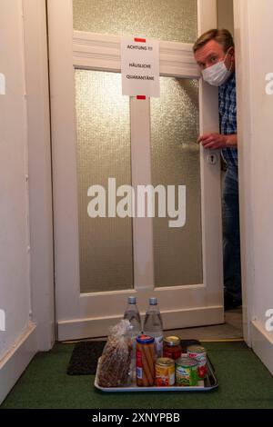 Immagine simbolica quarantena domestica, l'uomo è in isolamento a casa a causa di una sospetta infezione corona, segnale di avvertimento per i visitatori sulla porta d'ingresso Foto Stock