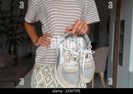 Primo piano di mani che tengono e ispezionano scarpe da ginnastica ben indossate, sottolineando la tendenza al consumo consapevole e alla sostenibilità Foto Stock