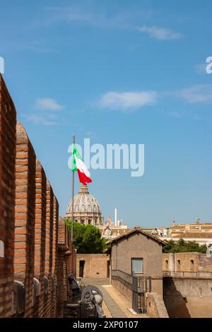 Roma, Italia - 2 agosto 2019: Basilica di San Pietro in Vaticano vista dal museo di Castel Sant'Angelo come la bandiera italiana ondeggia nel vento Foto Stock