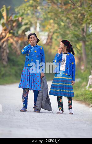 Due donne della minoranza hmong in abiti di tutti i giorni stanno in strada e coprono la bocca di risate, Du gia, provincia di ha Giang, Vietnam Foto Stock