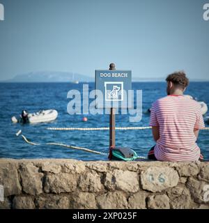 Firma con l'iscrizione Dog Beach in un campeggio a Krk, Croazia. Accanto ad esso, un villeggiante che riposa su un muro Foto Stock