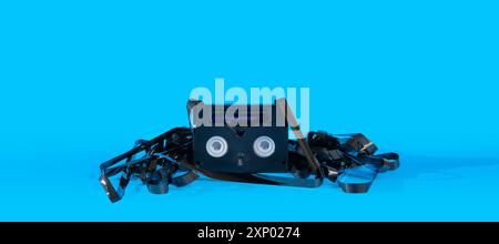Vecchia cassetta mini DV nera danneggiata con il nastro esterno che circonda la cassetta su sfondo blu Foto Stock