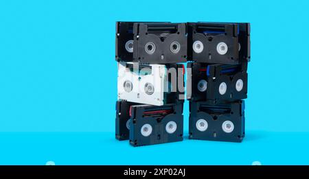 Vista frontale di una torre di vecchie cassette mini DV nere su una superficie blu su sfondo blu Foto Stock