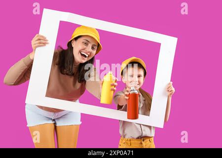 La bambina e sua madre hanno in mano lattine di vernice spray e cornice di carta su sfondo viola Foto Stock