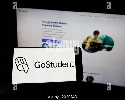 Stoccarda, Germania, 03-30-2022: Persona che tiene il cellulare con il logo della società austriaca di tutoraggio GoStudent GmbH sullo schermo davanti all'azienda Foto Stock