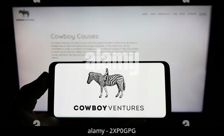 Stoccarda, Germania, 02-26-2022: Persona che detiene il cellulare con il logo della società americana di venture capital Cowboy Ventures sullo schermo davanti alla pagina web. Foto Stock