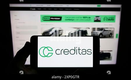 Persona che detiene lo smartphone con il logo della società brasiliana Creditas Solucoes Financeiras Ltda. sullo schermo davanti al sito web. Mettere a fuoco il display del telefono Foto Stock