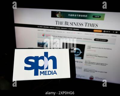 Stoccarda, Germania, 02-11-2022: Persona che tiene un cellulare con il logo della società singaporiana SPH Media Limited sullo schermo davanti al Business Times Foto Stock