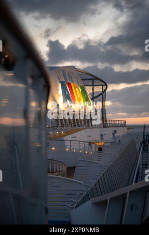 Logo AIDA illuminato applicato alla nave AIDA bella con recinzione e ponte della barca davanti la sera, scatto verticale Foto Stock