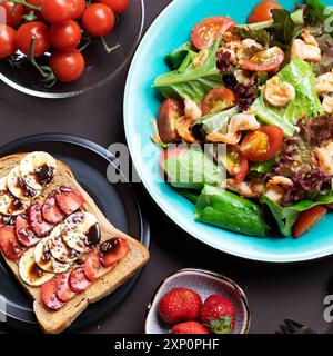 Una colazione vivace e allettante con insalata colorata, gamberi, pomodori maturi, sandwich, banane, fragole fresche. Un pasto salutare offre un delizioso nutri Foto Stock