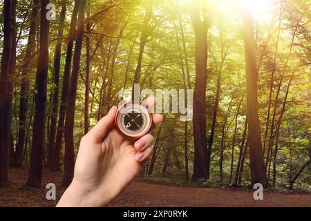 Donna che tiene la bussola vicino al sentiero nella foresta illuminata dal sole, primo piano Foto Stock